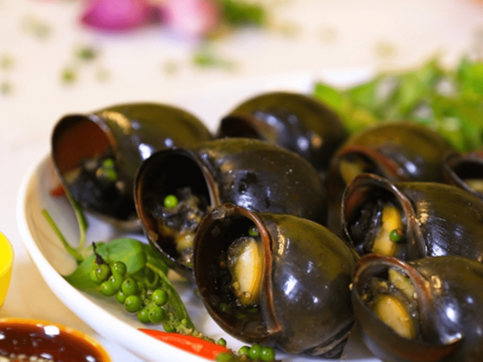 A close-up of snails steamed with lemongrass at Ốc Loan, served with fresh herbs and seafood sides.