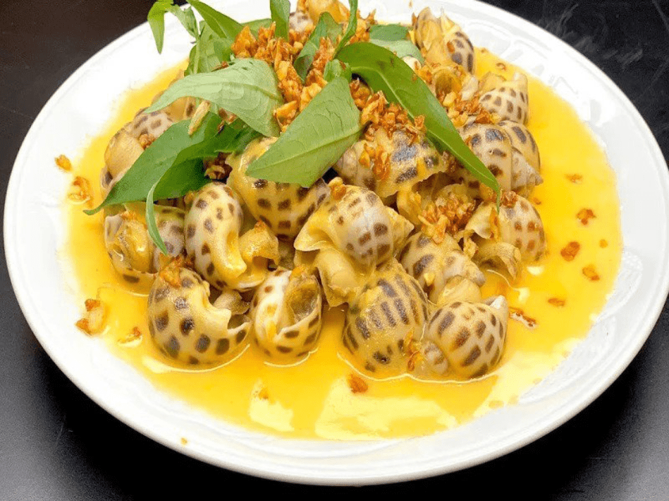 A close-up of snails with salted egg yolk sauce at Ốc Năm, alongside grilled seafood.