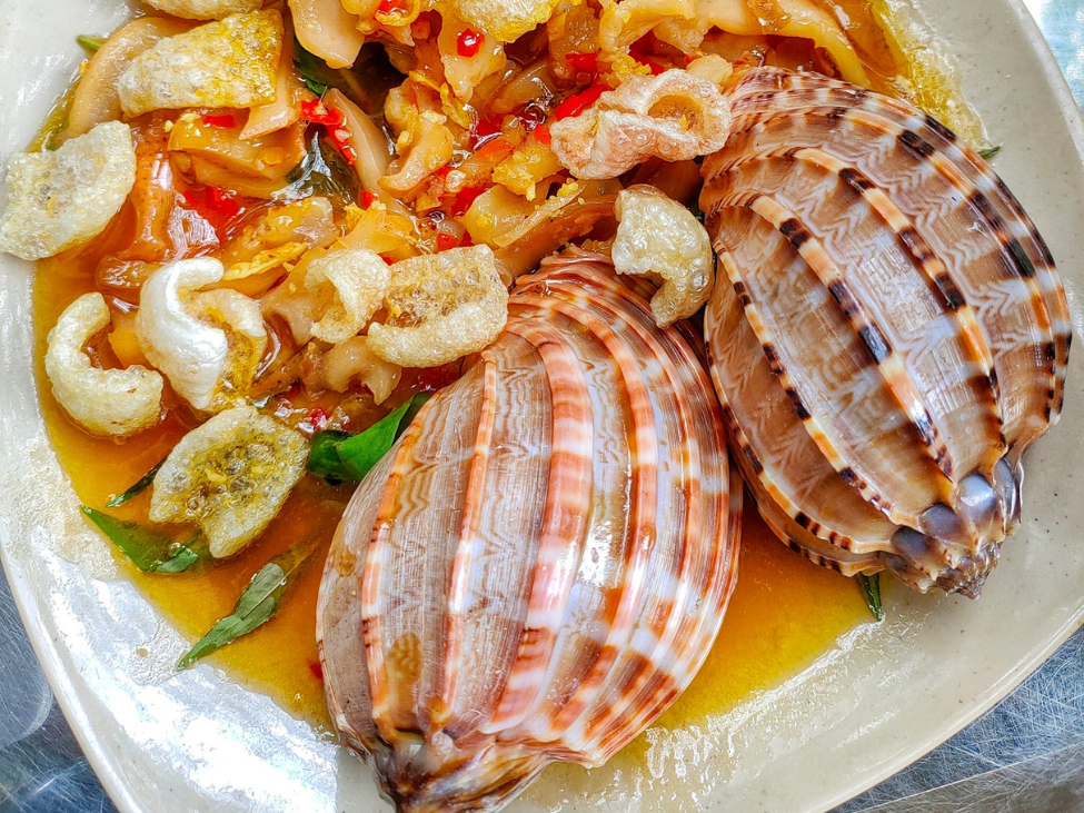 A plate of stir-fried snails with tamarind sauce at Ốc Oanh, served with fresh vegetables and grilled prawns.