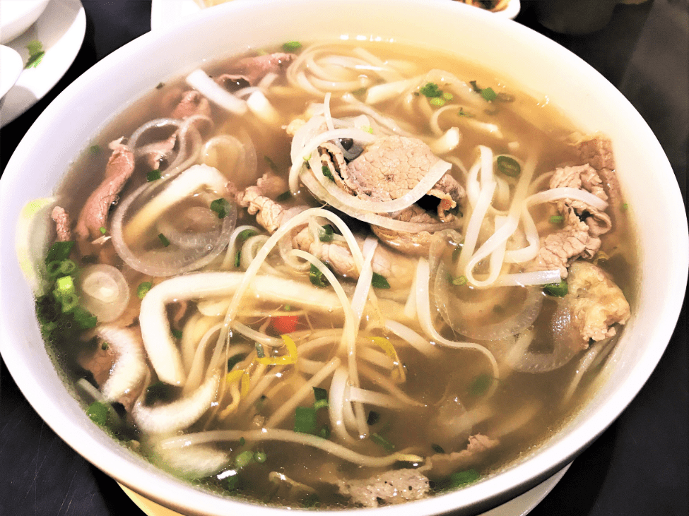 A bowl of Pho 2000's famous pho served with fresh herbs and lemon wedges.