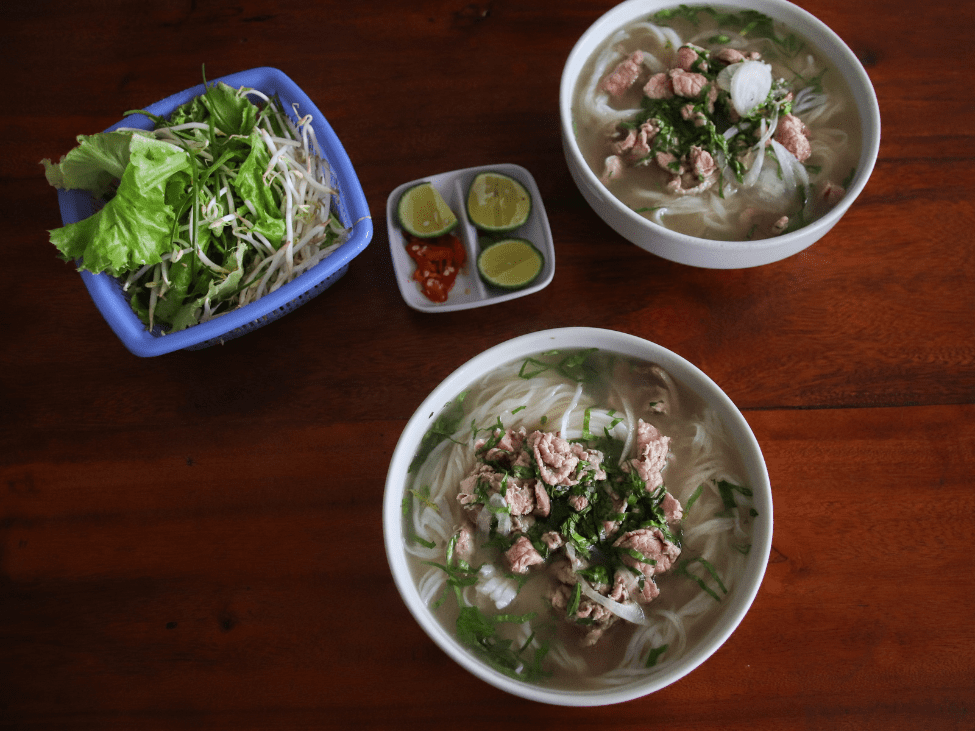 Pho Binh's traditional pho bowl served with fresh herbs and lime slices.