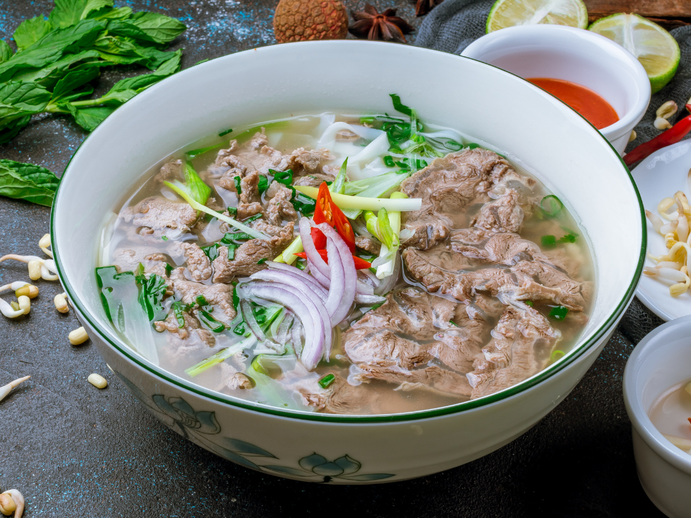 A steaming bowl of beef pho with fresh herbs and lime.