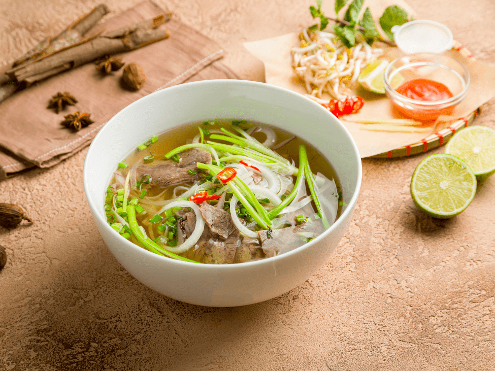 A plate of fresh herbs, lime, and chili slices ready to be added to a bowl of pho.