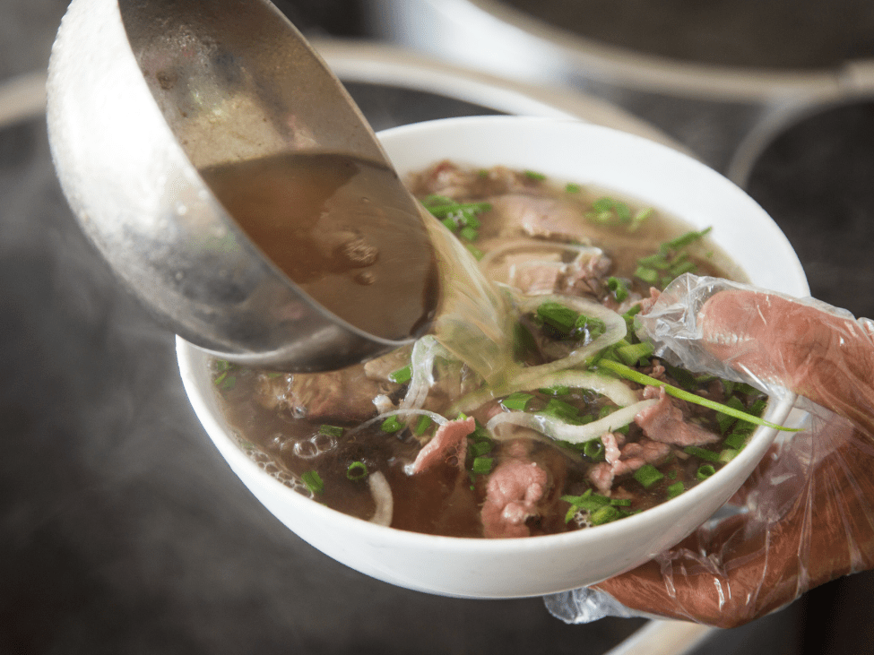 A steaming bowl of Pho with herbs and lime, ready to eat