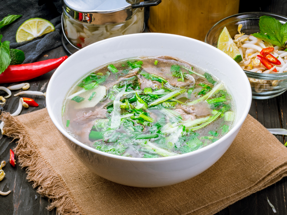 A bowl of Pho Hanoi with a clear broth, thin rice noodles, and green onions.