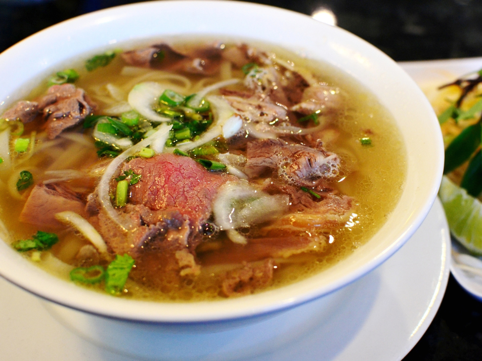 A bowl of Pho Hoa Pasteur's beef pho with fresh herbs and lime wedges.