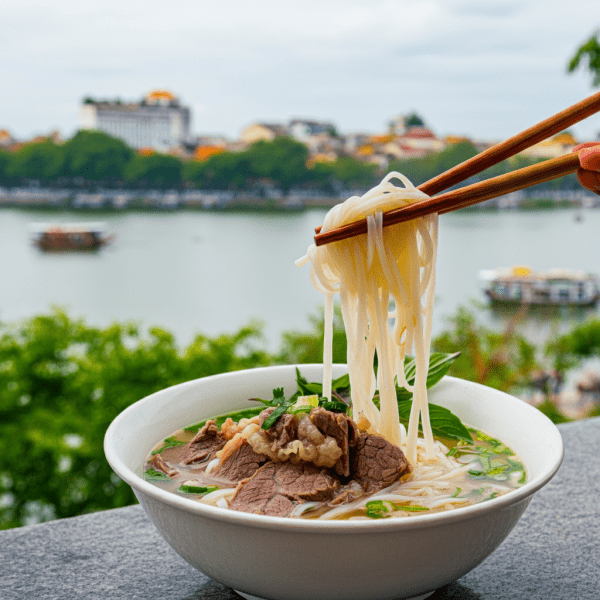 A bowl of Phở Lâm with a picturesque view of Hoan Kiem Lake in the background.