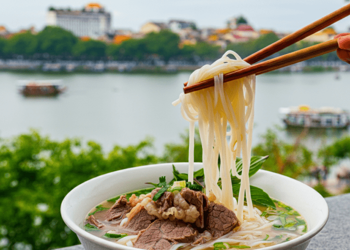 A bowl of Phở Lâm with a picturesque view of Hoan Kiem Lake in the background.