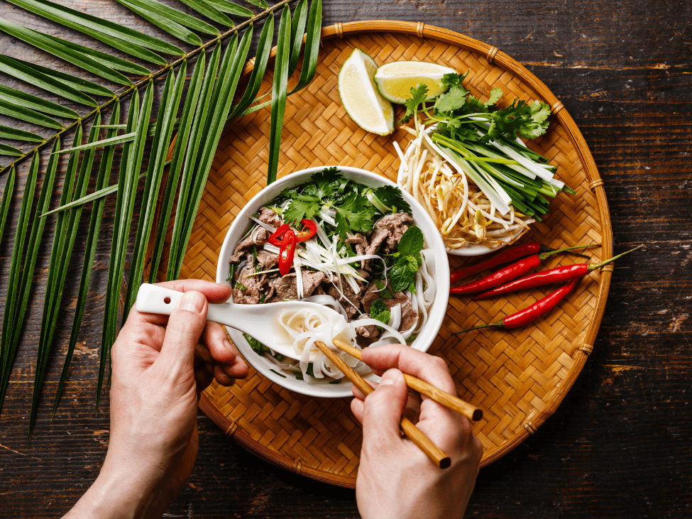 A person using chopsticks to lift noodles from a steaming bowl of pho.