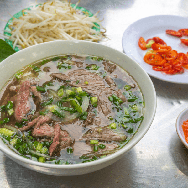 A colorful bowl of Pho Saigon with bean sprouts, basil, and hoisin sauce.