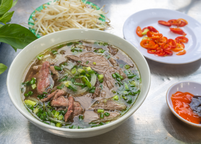 A colorful bowl of Pho Saigon with bean sprouts, basil, and hoisin sauce.