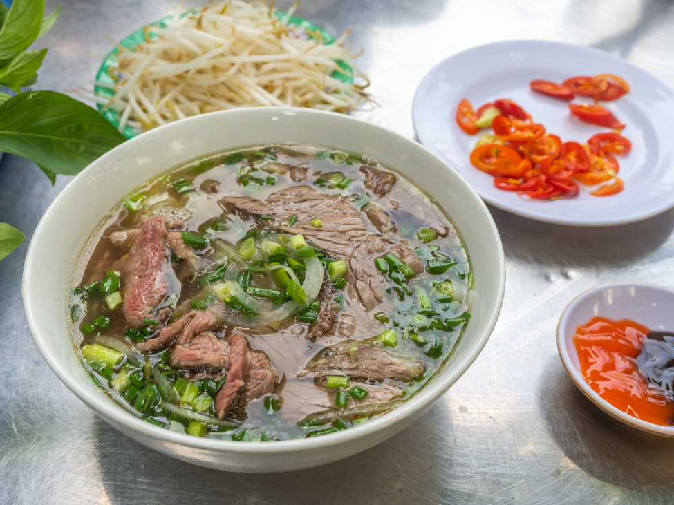 A colorful bowl of Pho Saigon with bean sprouts, basil, and hoisin sauce.