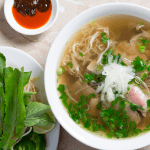 A vibrant bowl of pho saigon vietnamese with various herbs and bean sprouts.