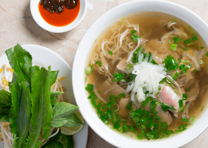 A vibrant bowl of pho saigon vietnamese with various herbs and bean sprouts.