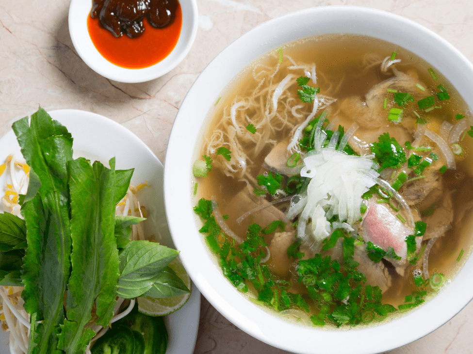 A vibrant bowl of pho saigon vietnamese with various herbs and bean sprouts.