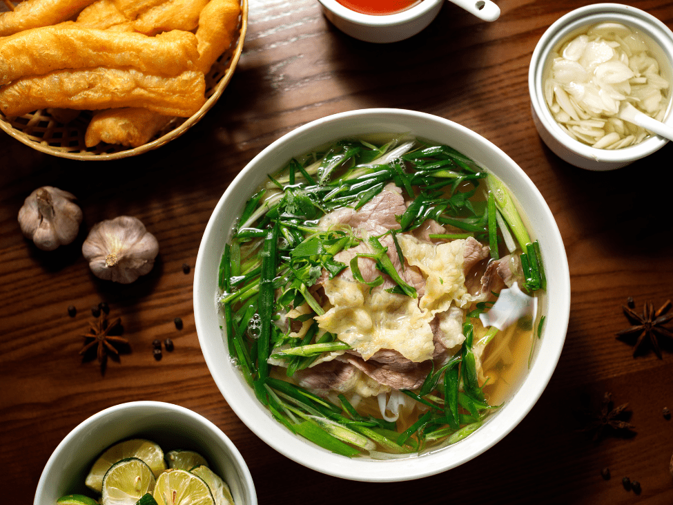 A side dish of fried dough sticks and beef meatballs served alongside a bowl of pho.