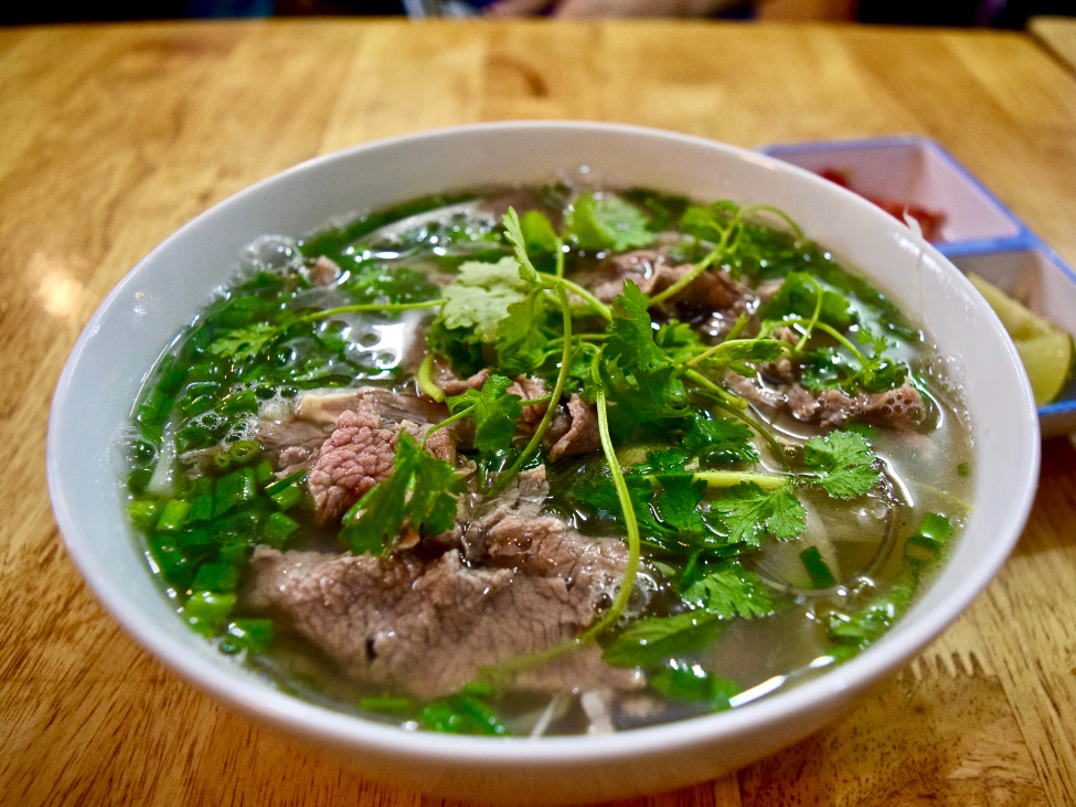 A bowl of Saigon pho filled with fresh herbs, chili peppers, and lime.