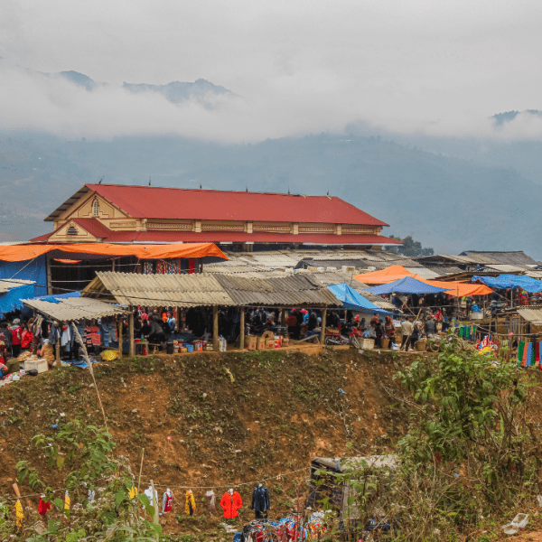 A bustling market in Sapa with ethnic minority women in traditional clothing selling handmade crafts.