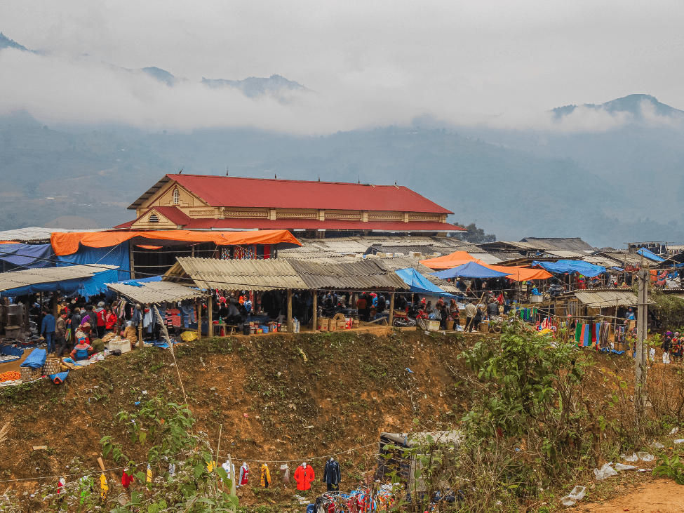 A bustling market in Sapa with ethnic minority women in traditional clothing selling handmade crafts.