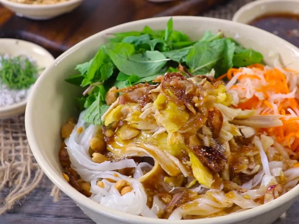 A bowl of sour pho with pork, pickled vegetables, and herbs.