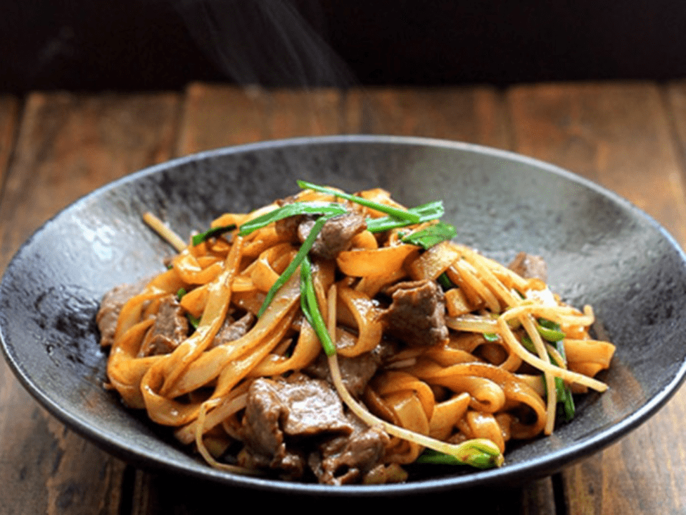 Stir-fried pho noodles with beef and vegetables in a bowl.