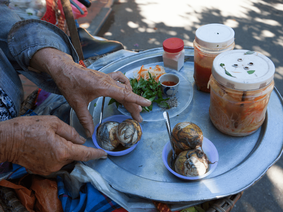 A street vendor in Saigon preparing Hot Vit Lon with various condiments on display.