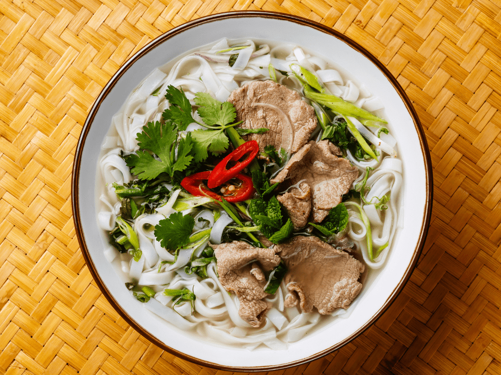 A bowl of traditional Vietnamese pho topped with herbs, lime, and chili.