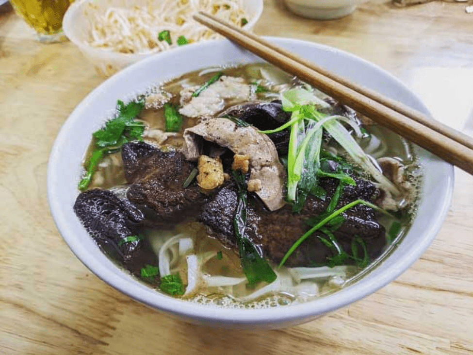 A bowl of Phở Gan Cháy with charred liver, herbs, and flavorful broth.