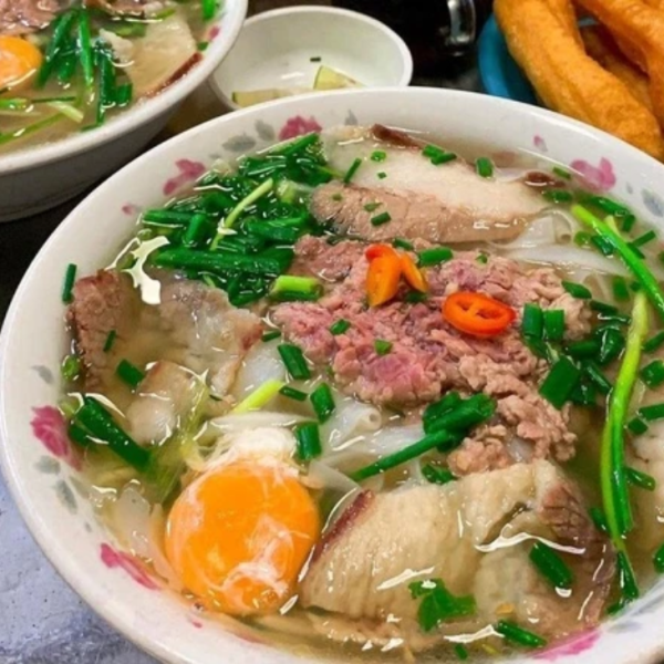 A bowl of pho with unique toppings like quail eggs, fried shallots, and pickled garlic.