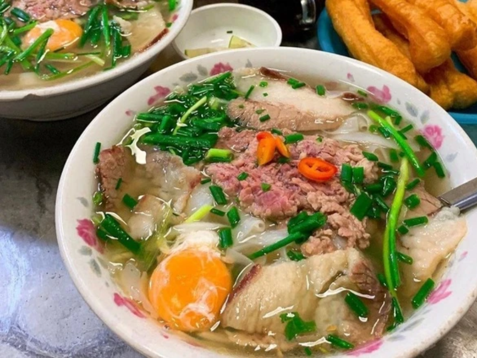 A bowl of pho with unique toppings like quail eggs, fried shallots, and pickled garlic