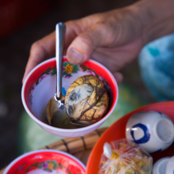 Close-up image of a Vietnamese balut egg with a partially developed embryo visible, served with salt, pepper, and fresh herbs.