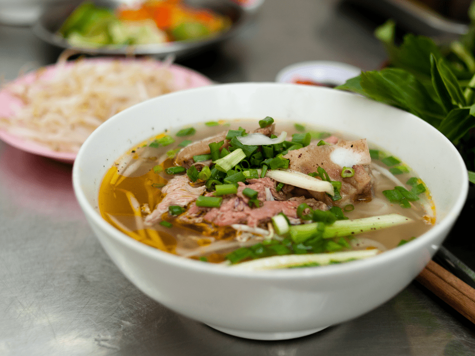 A steaming bowl of Vietnamese Phở with beef, herbs, and rice noodles.