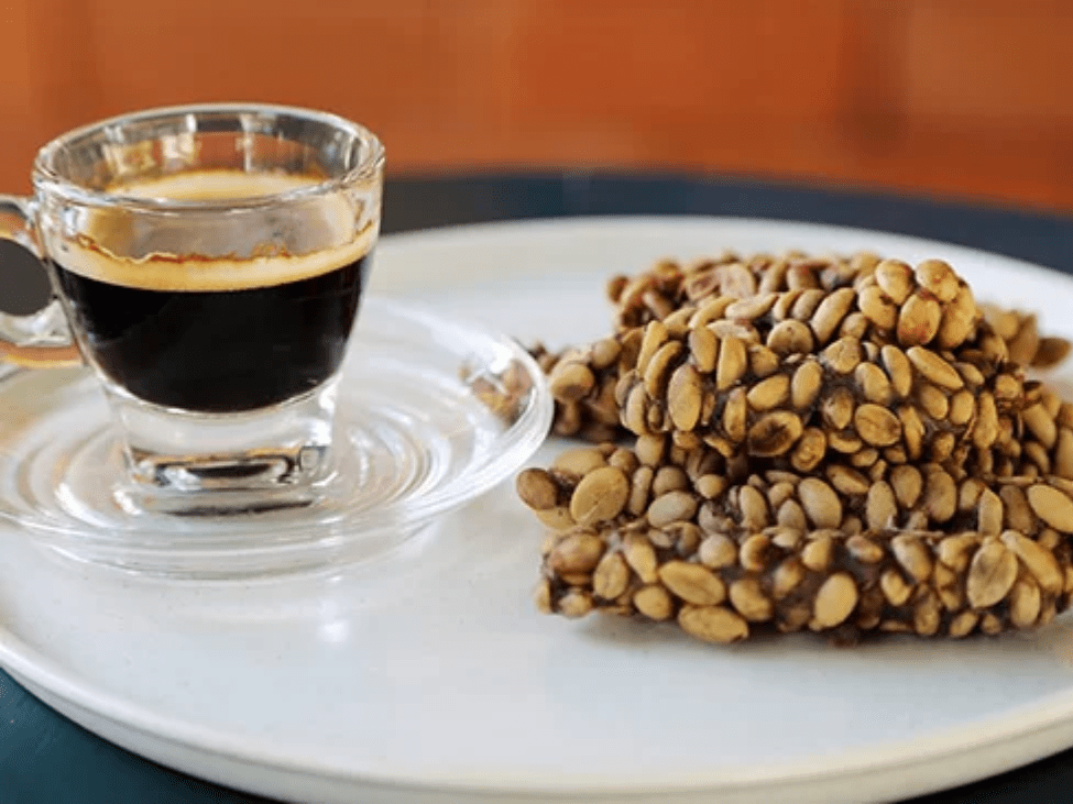 A cup of weasel coffee served with a small coffee filter on a wooden tray with beans on the side.