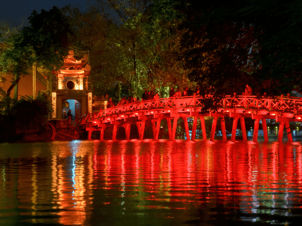 Huc Bridge and Ngoc Son Temple illuminated at night on Hoan Kiem Lake.