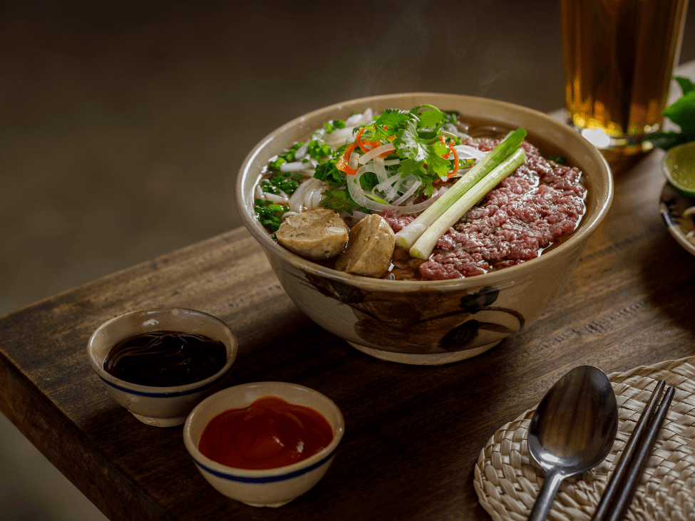 A steaming bowl of Vietnamese pho with fresh herbs and beef slices.