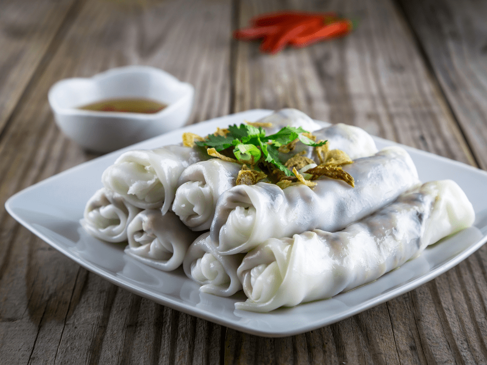 Banh Cuon rice rolls served with herbs and dipping sauce.