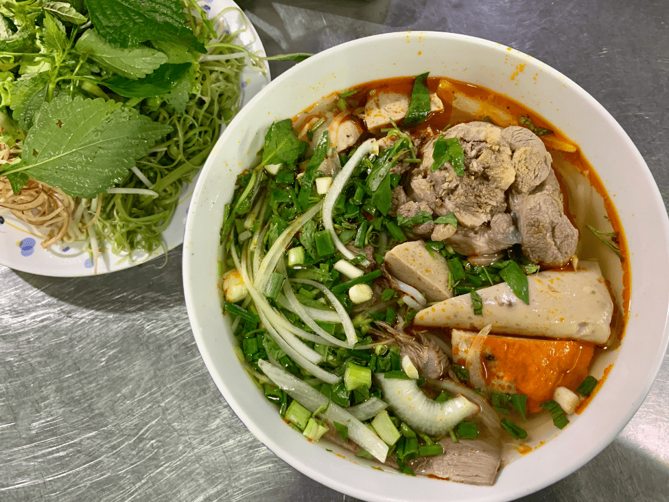 Spicy Bun Bo Hue noodle soup with herbs and chili oil.