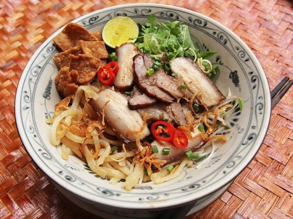 A bowl of Cao Lau noodles with pork and greens.