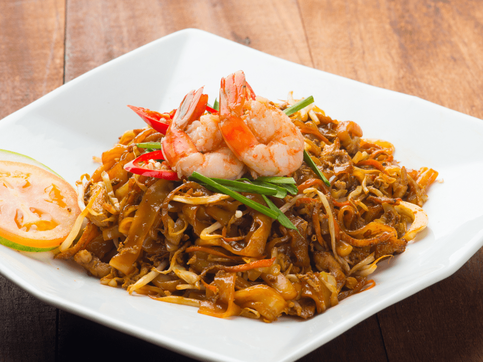 A plate of char kway teow stir-fried with prawns, Chinese sausage, and bean sprouts, served on a banana leaf.