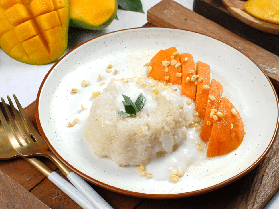 Mango sticky rice served with a drizzle of coconut sauce and a side of fresh mango slices.