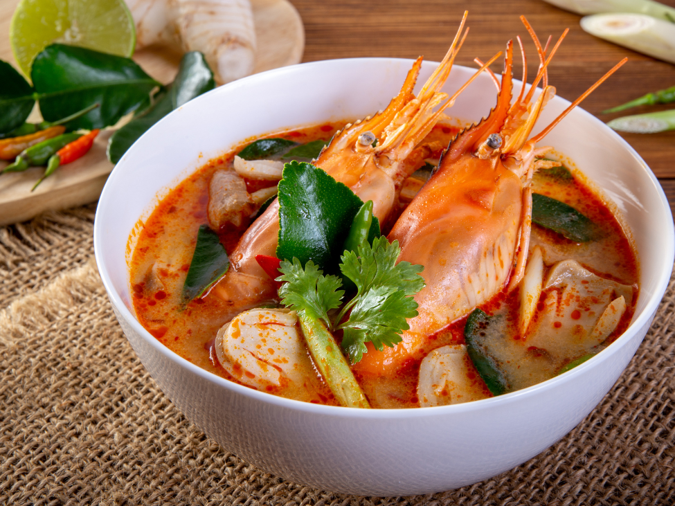 A bowl of Thai tom yum soup garnished with cilantro and lime wedges.