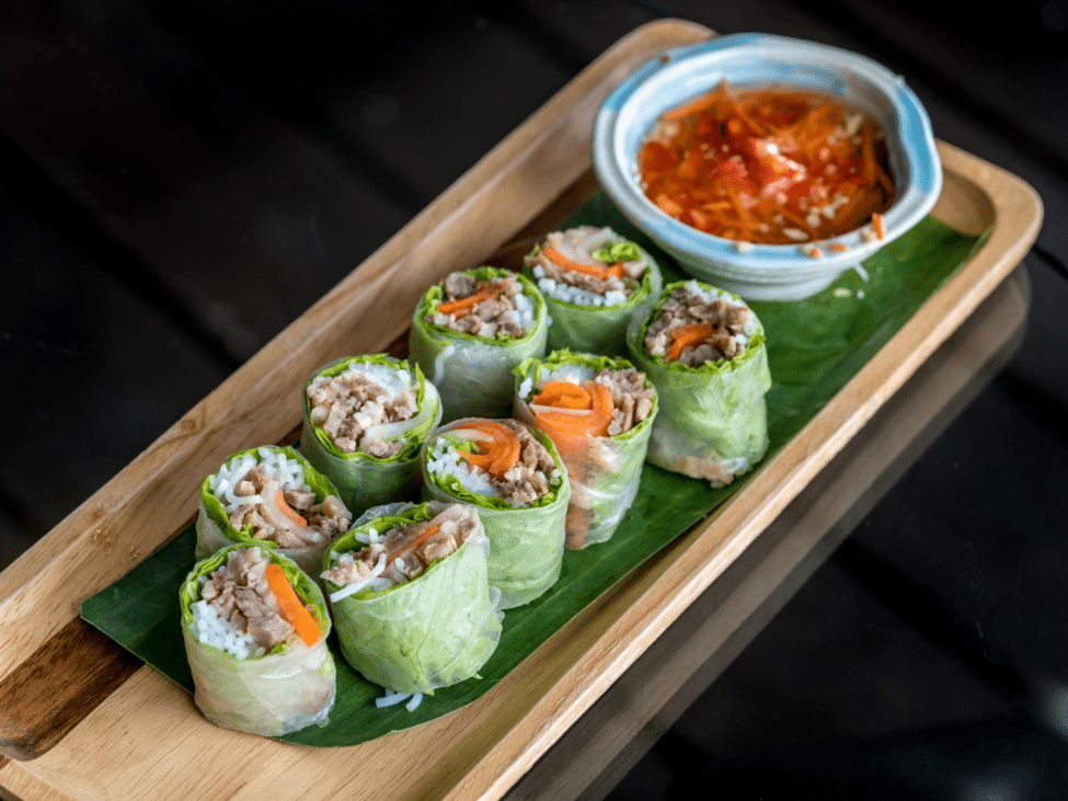 Vietnamese fresh spring rolls served with peanut dipping sauce on a bamboo platter.