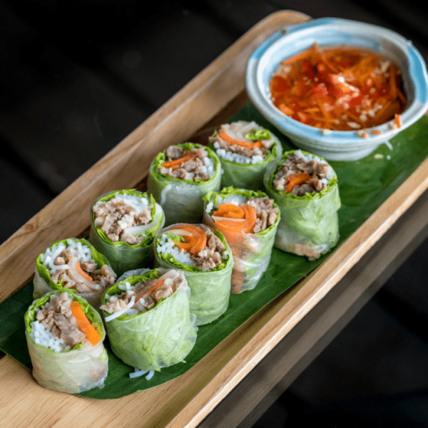 Vietnamese fresh spring rolls served with peanut dipping sauce on a bamboo platter.