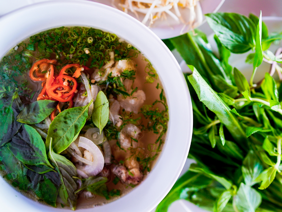 A steaming bowl of Vietnamese pho with beef, herbs, and lime.